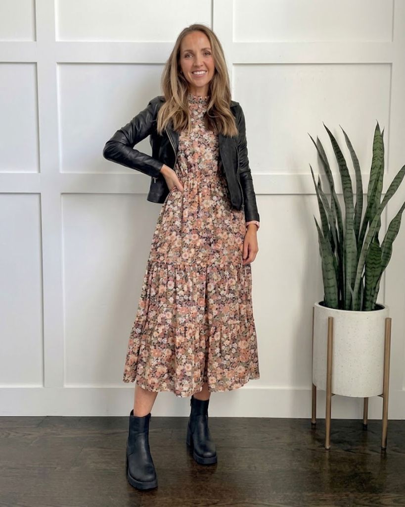 Woman smiling in a floral midi dress styled with a black leather biker jacket and Rieker Izzy black ankle boots.